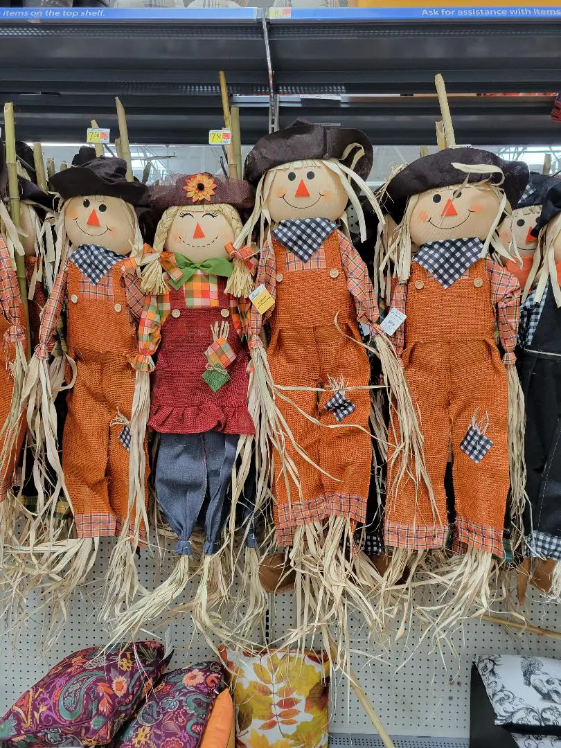 Four scarecrows dressed in orange overalls and hats, hanging side by side.
