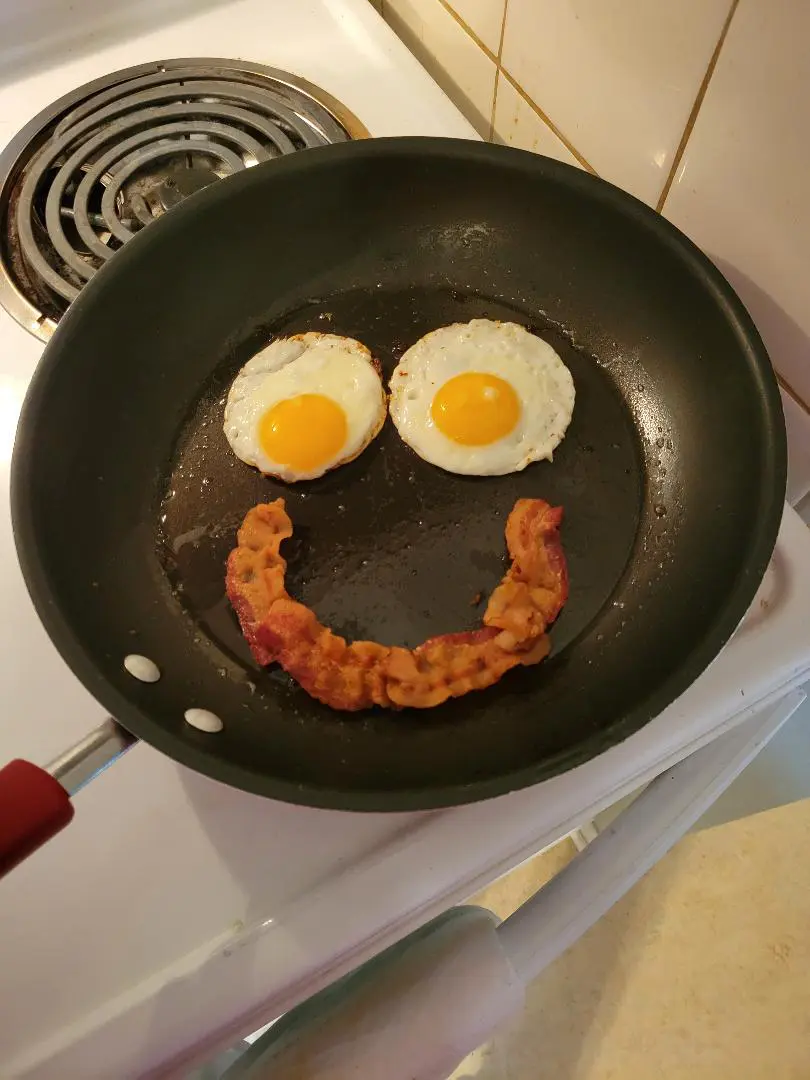 Sunny-side up eggs and bacon arranged as a smiling face in a frying pan.