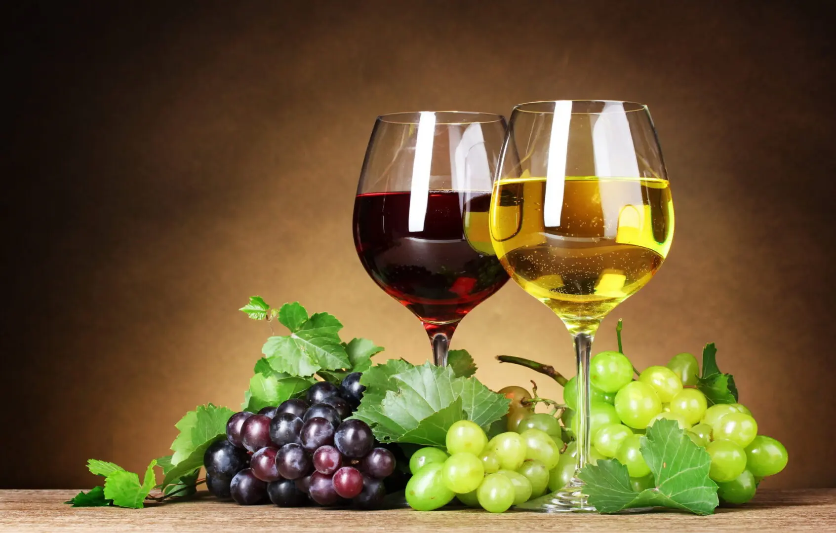 Two glasses of wine with green and purple grapes beside them.