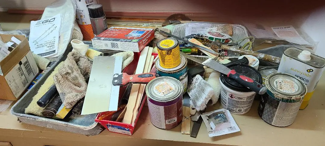 Cluttered workbench with paint cans, brushes, and various tools.